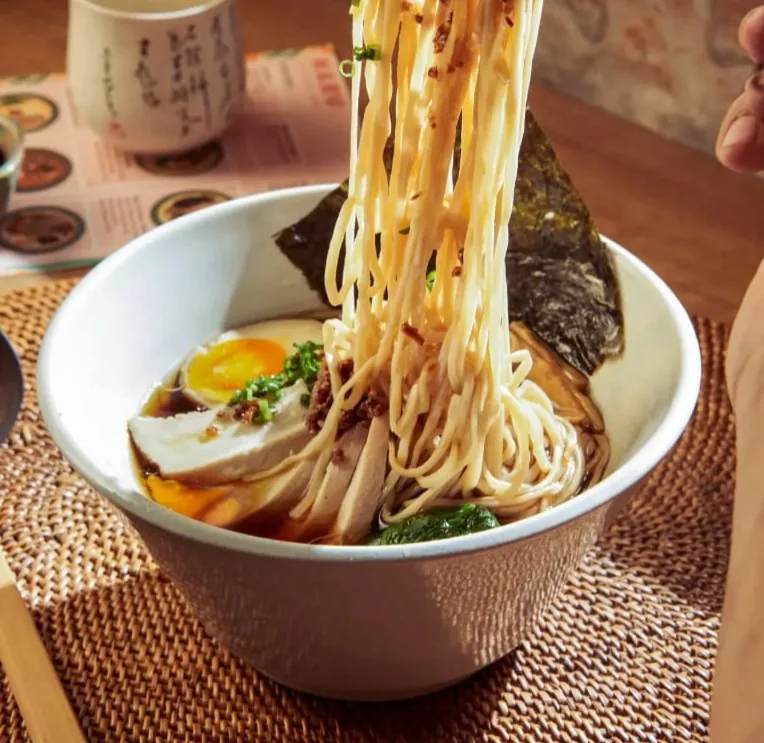 箸で麺を持ち上げた半熟卵入りのラーメン